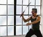 Adult man using VR headset and nunchaku for martial arts training indoors, exploring futuristic technology.