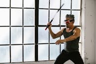 Adult man using VR headset and nunchaku for martial arts training indoors, exploring futuristic technology.